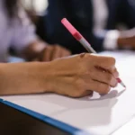 Seseorang menulis dokumen proposal bisnis di atas meja kerja