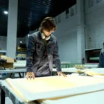 Pekerja pabrik berseragam sedang memeriksa lembar produksi di lingkungan manufaktur yang terang, menggambarkan proses pengendalian kualitas SPC